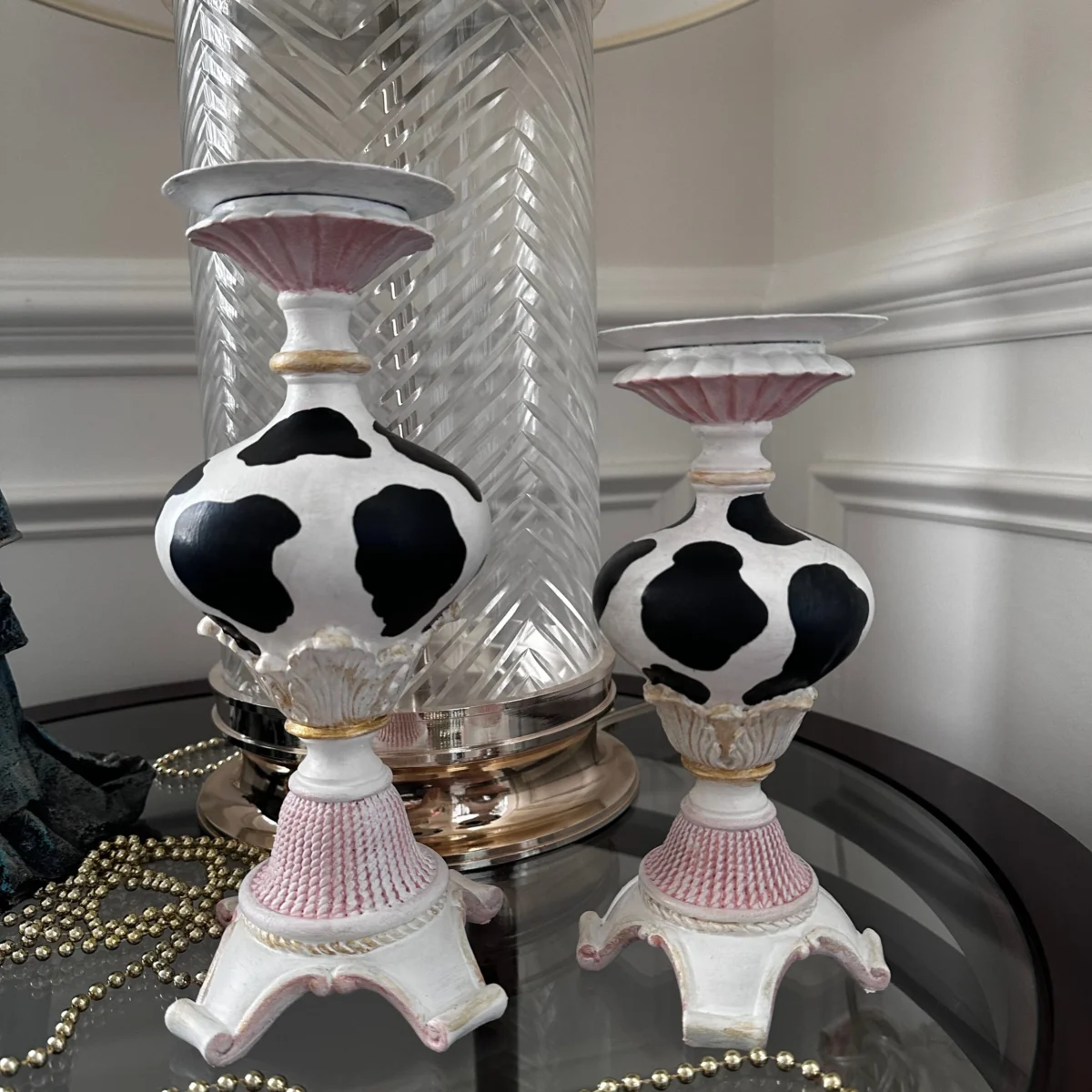 Hand-painted metal candle holders featuring a black and white cow pattern, inspired by vintage designs, perfect for adding a classic touch to any decor