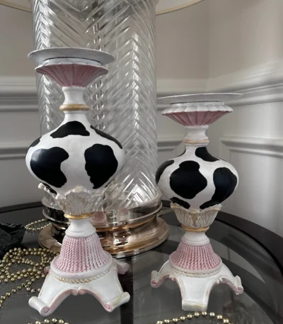 Hand-painted metal candle holders featuring a black and white cow pattern, inspired by vintage designs, perfect for adding a classic touch to any decor